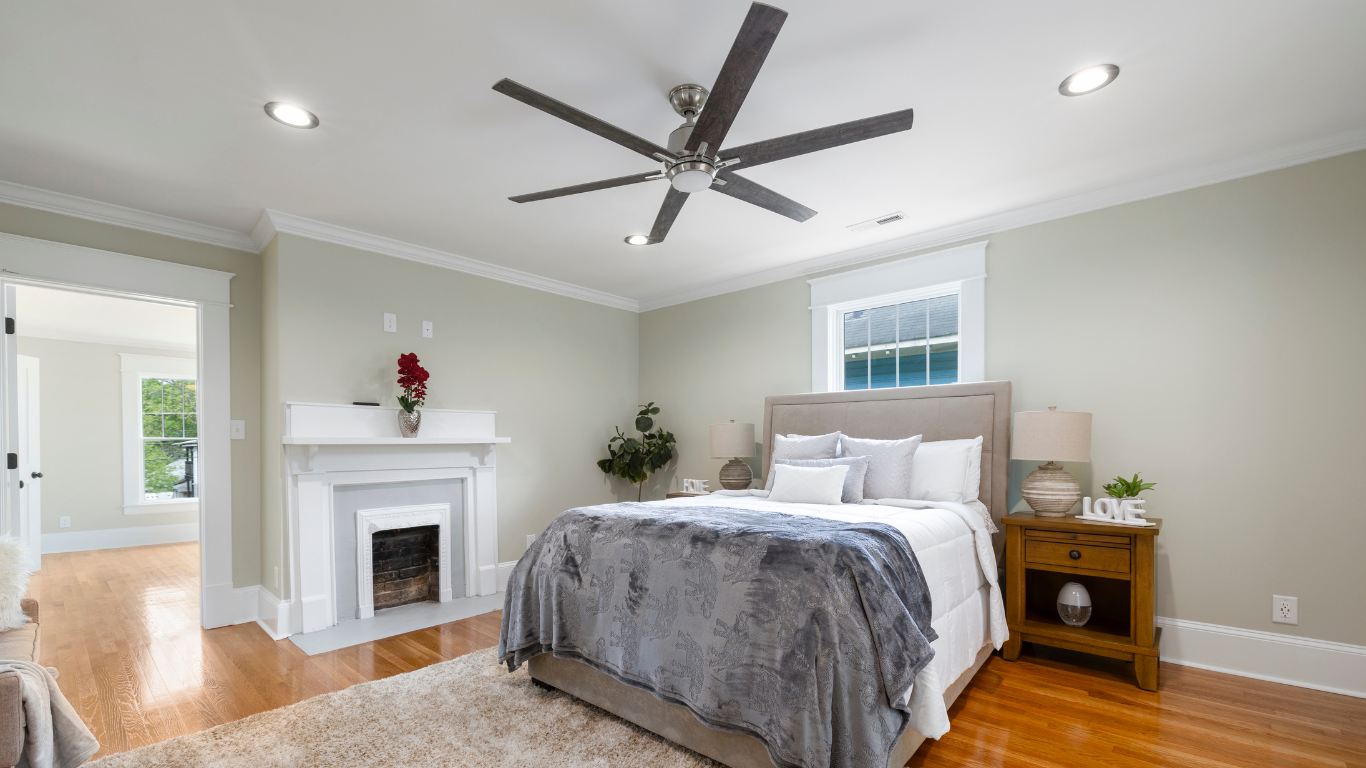 Bedroom with bed, fireplace, wooden floor, gray walls, and ceiling fan.