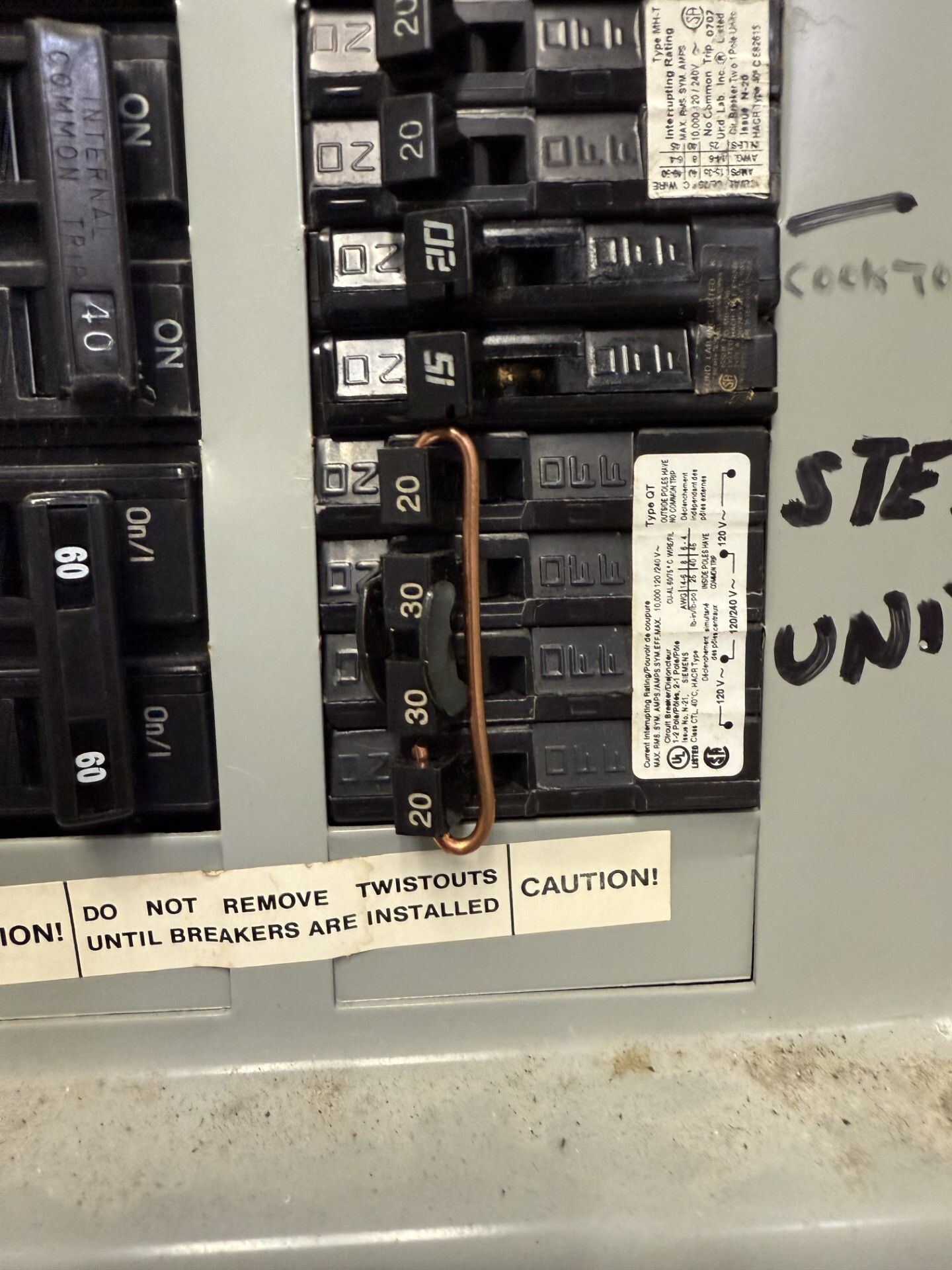 Electrician in yellow gloves using multimeter on a circuit breaker panel.