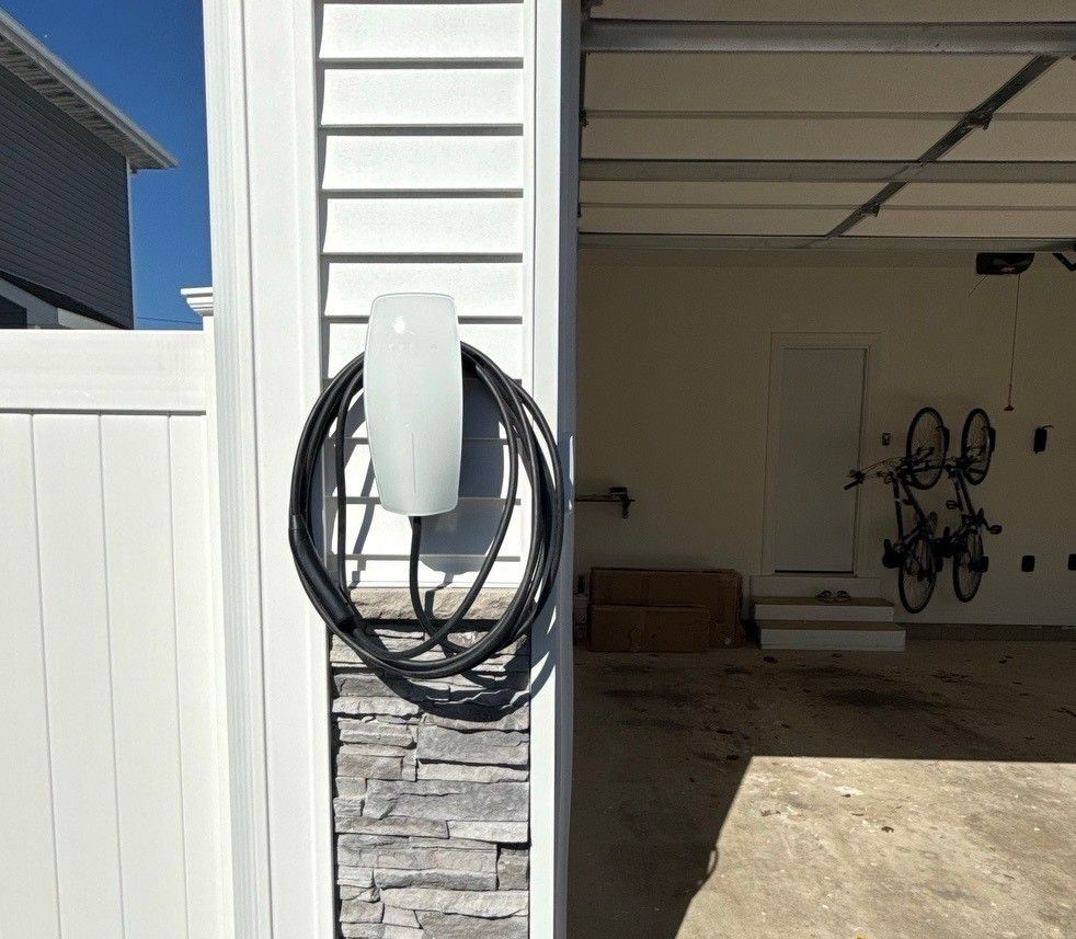 White electric car charging; woman in casual attire enters house.