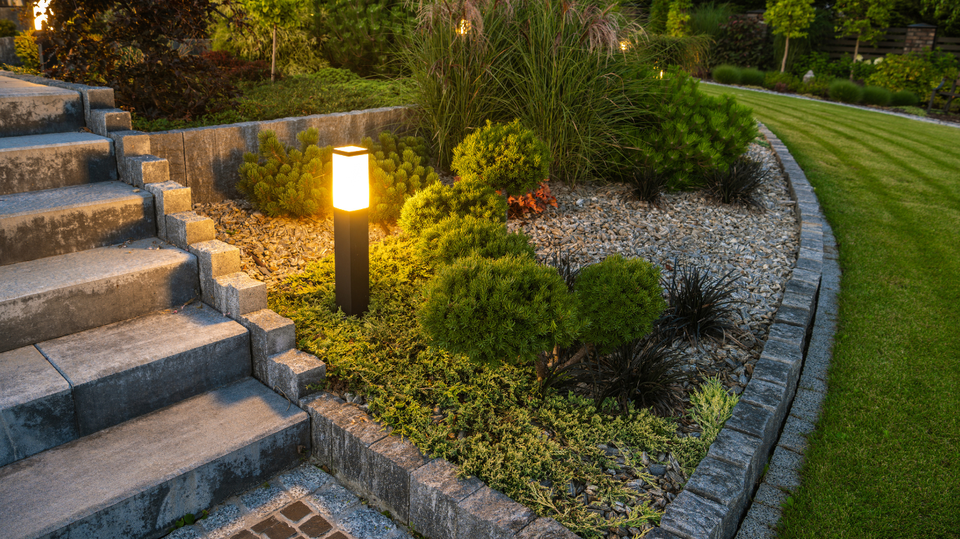 Stone steps and landscaped garden illuminated by a lamp at dusk.