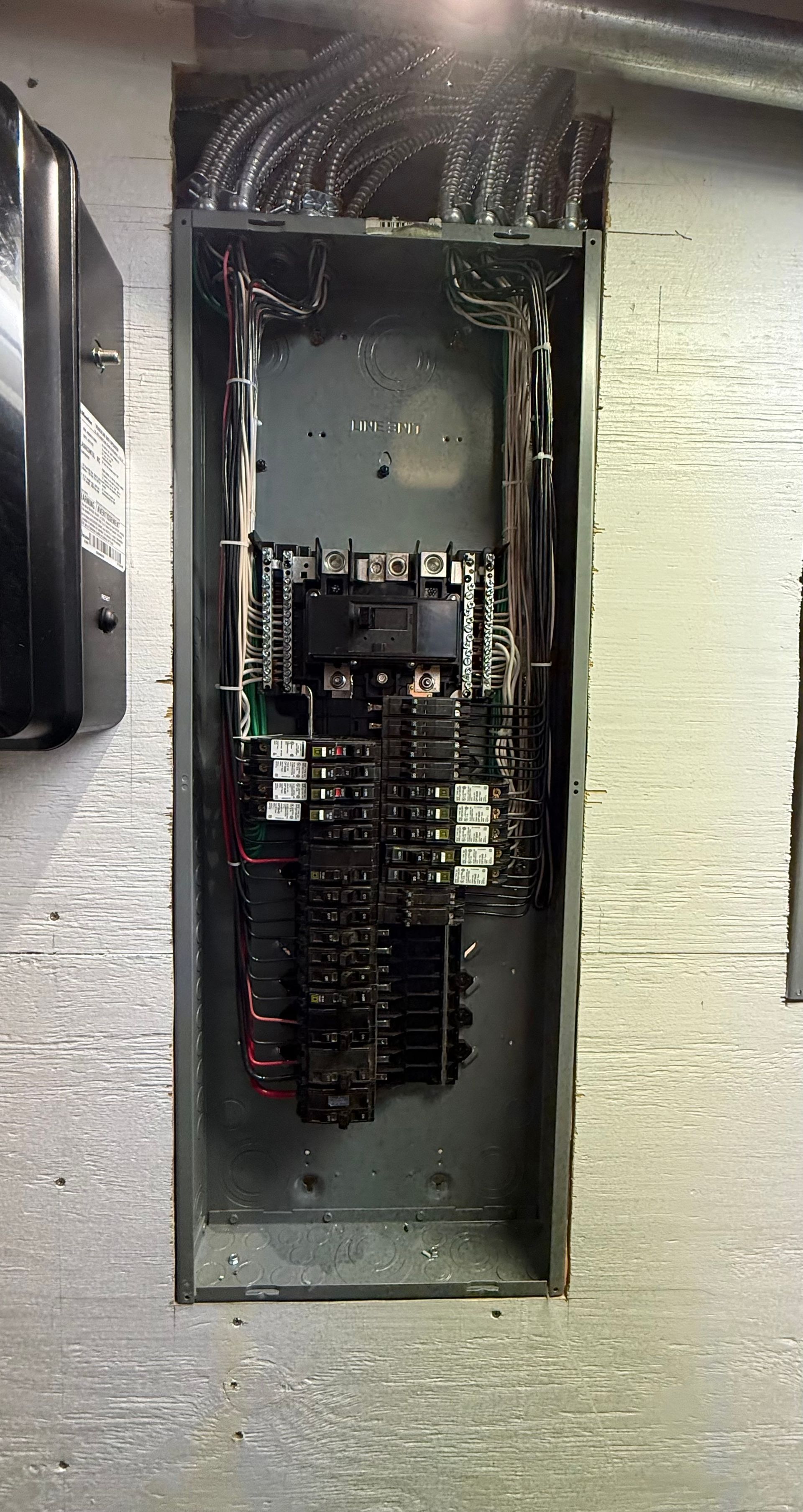 Electrician in hard hat and safety glasses using a multimeter on an electrical panel.