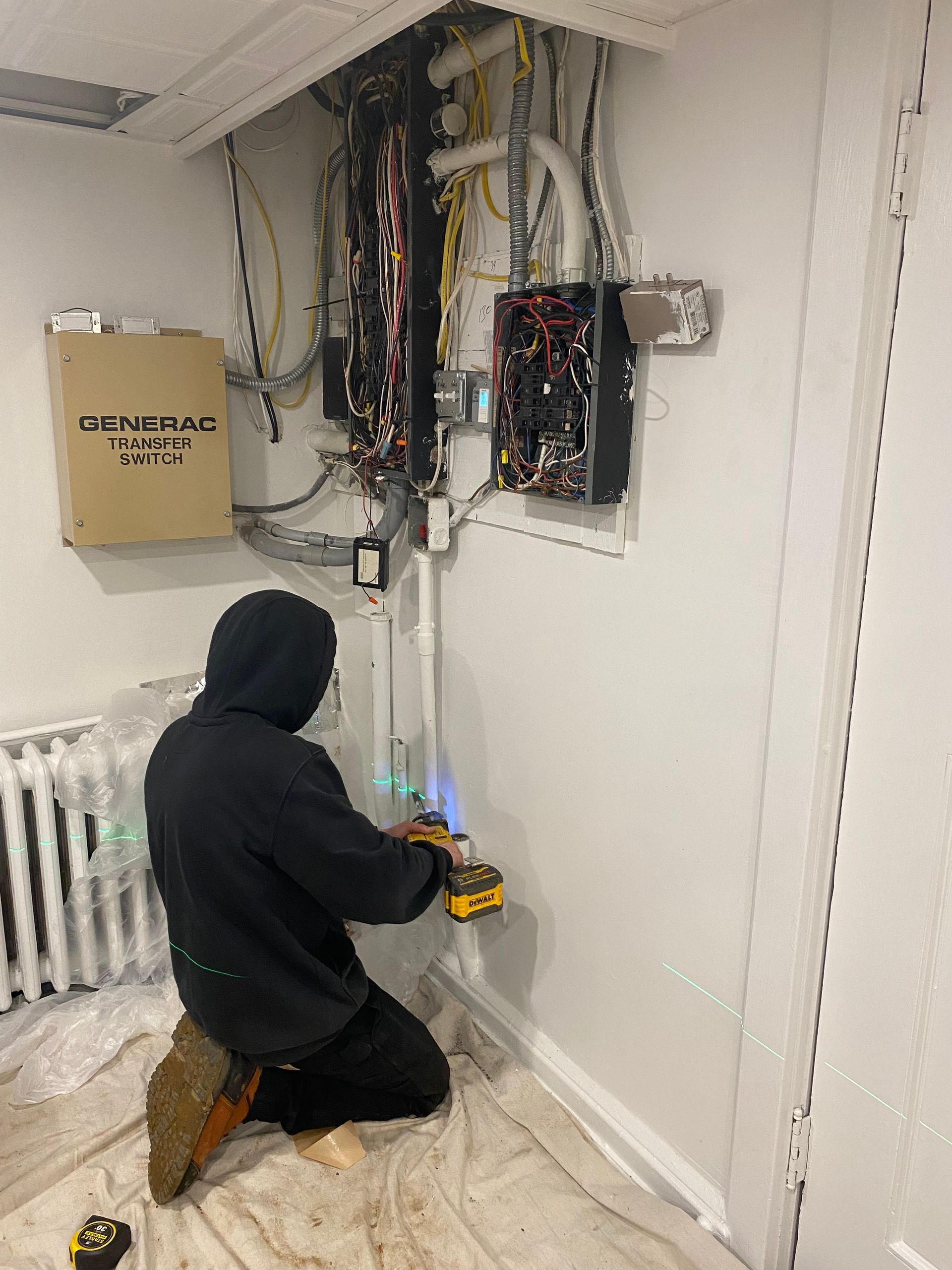 Electrician with hard hat and safety glasses working on ceiling wires.