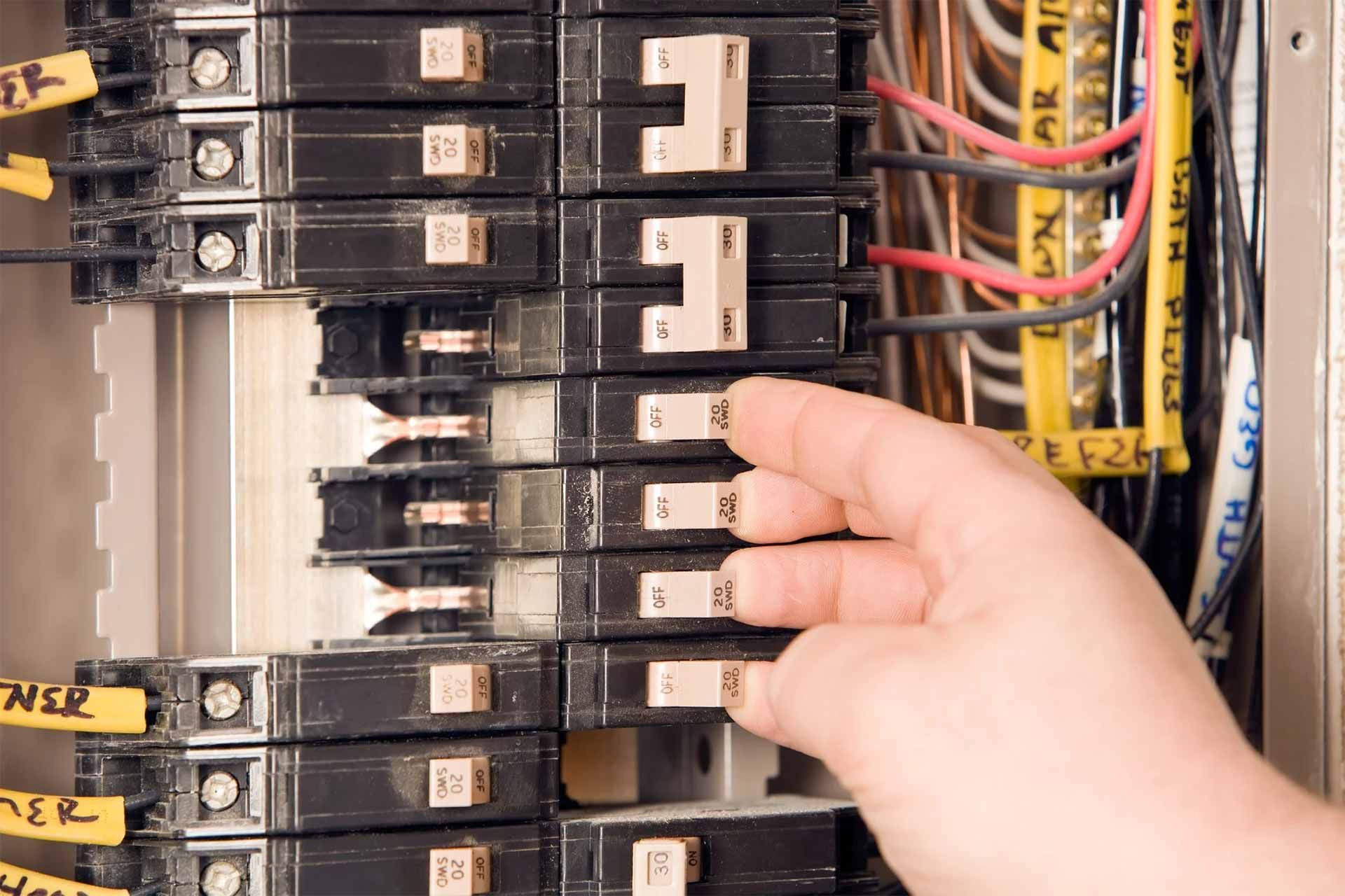 Hand turning off a circuit breaker in an electrical panel.