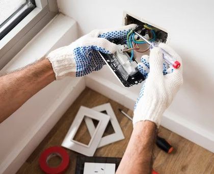 Electrician in gloves working on wiring in a wall outlet, indoor setting.
