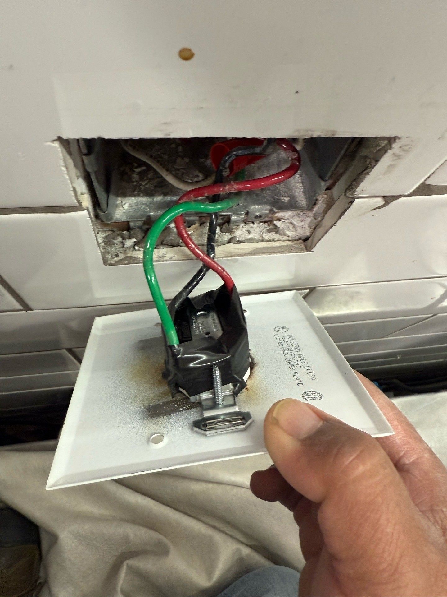 Electrician installing an outlet on a brick wall. He is wearing a white hard hat and safety glasses.