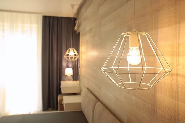 Modern bedroom with wireframe pendant lights, wooden wall, curtains, and a bed.