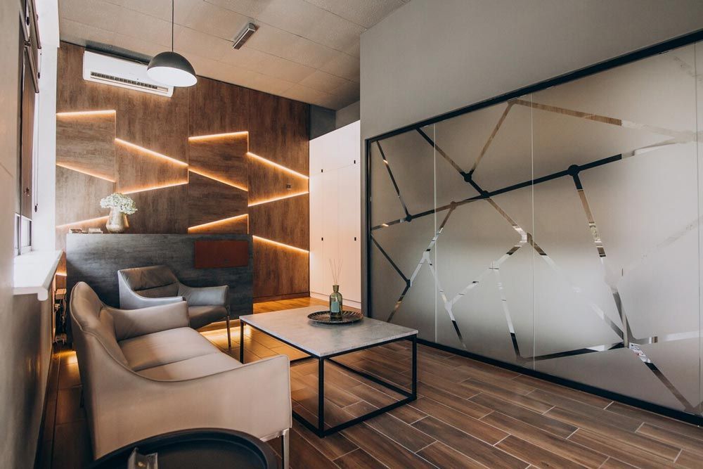 Cozy waiting room with modern design: wood paneling, sofa, frosted glass wall, and accent lighting.