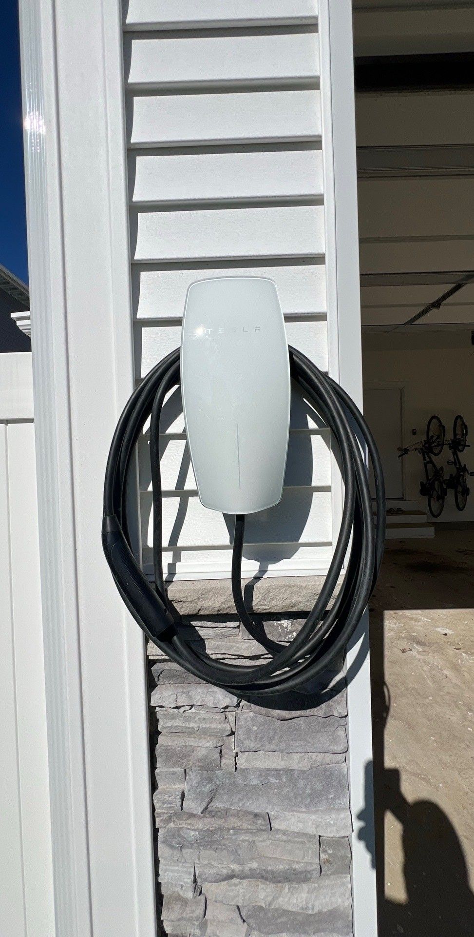 Electric vehicle charging station on a wall outdoors with a green lawn background.