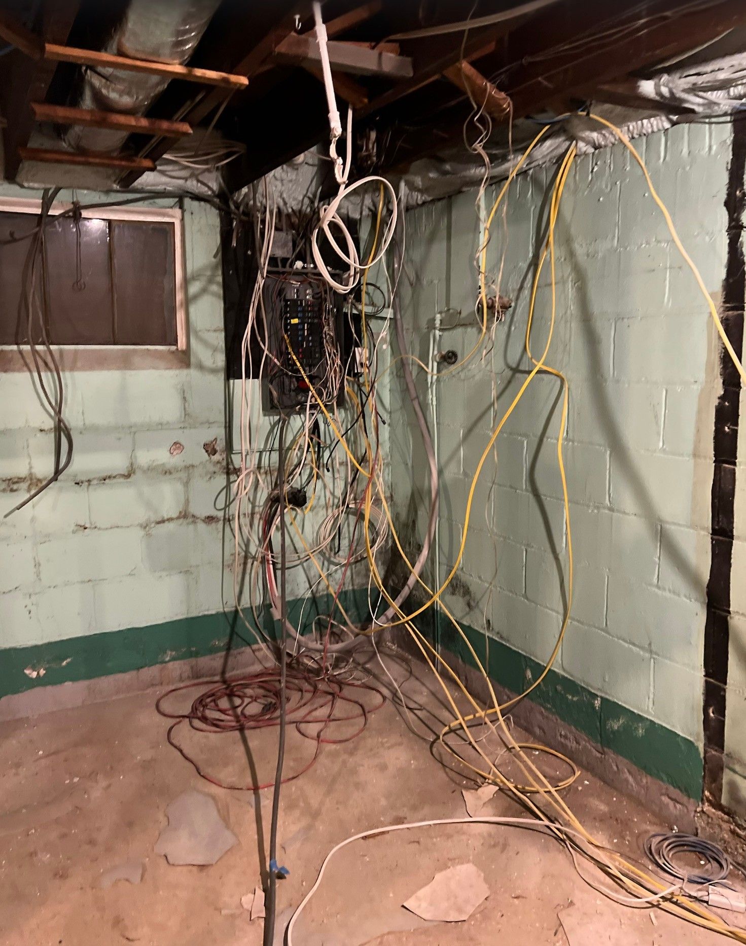 Electrician working on wiring; wearing tool belt, standing near concrete wall with a ladder.