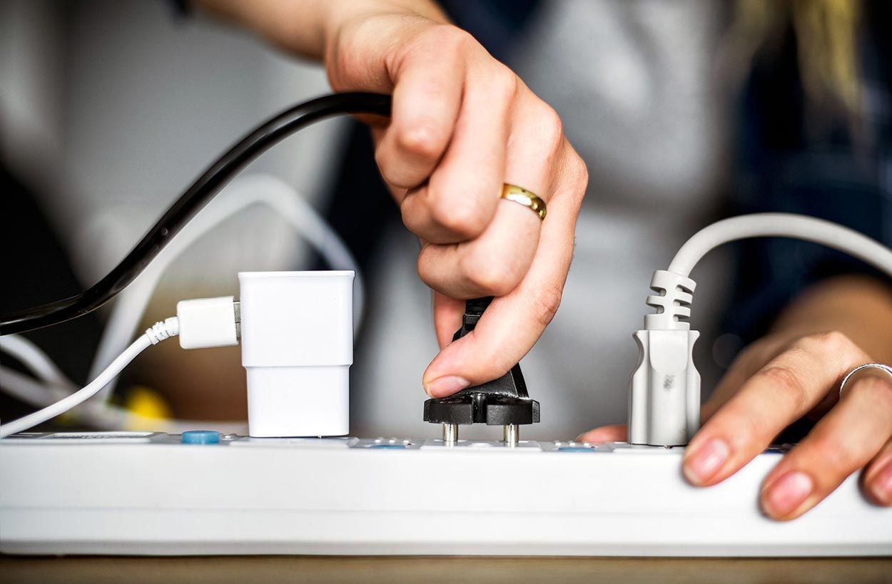 Person plugging a black power cord into a white power strip with other cords plugged in.