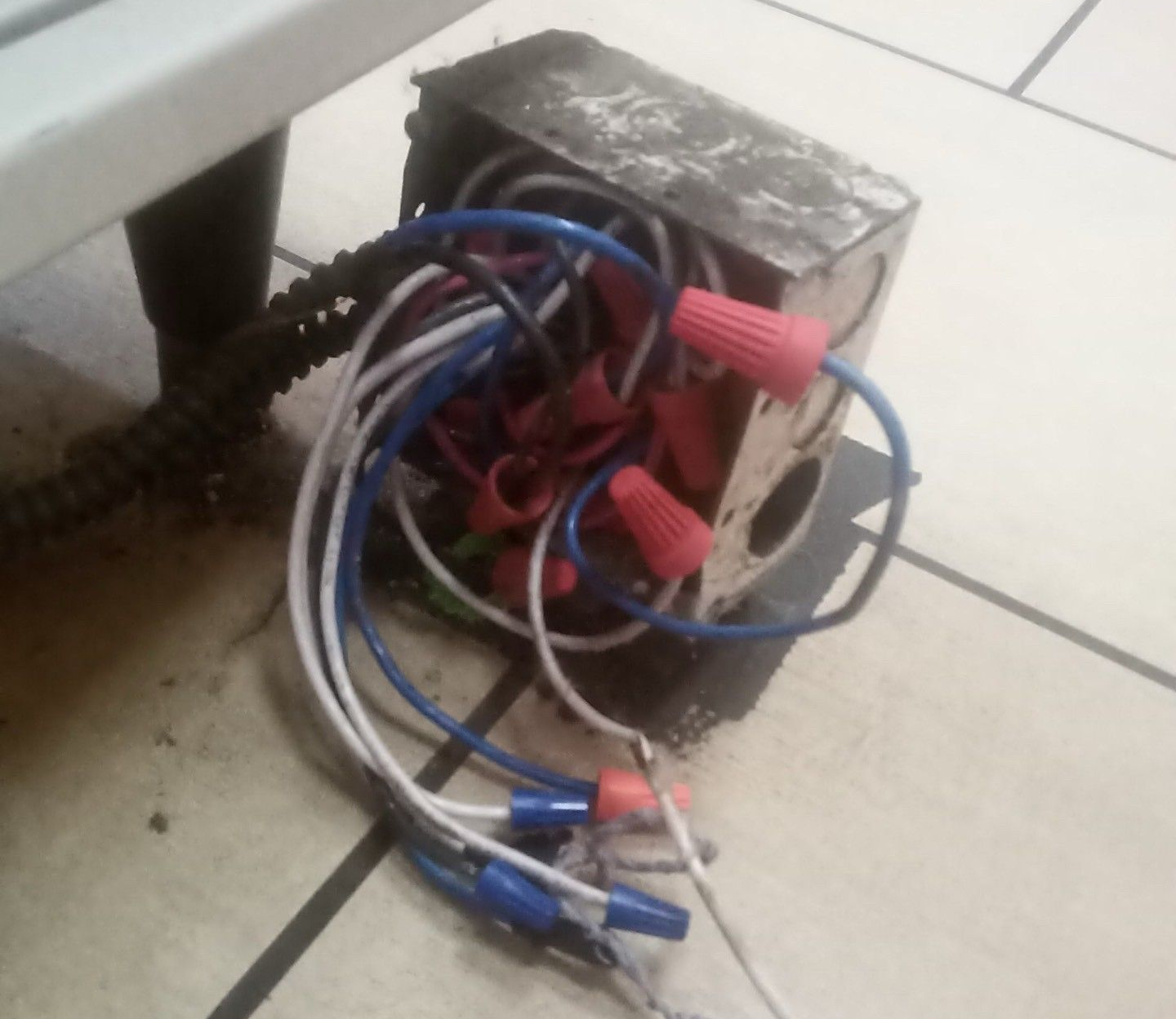 Hand plugging a black power cord into a white wall outlet with USB ports, on a light wood grain wall.