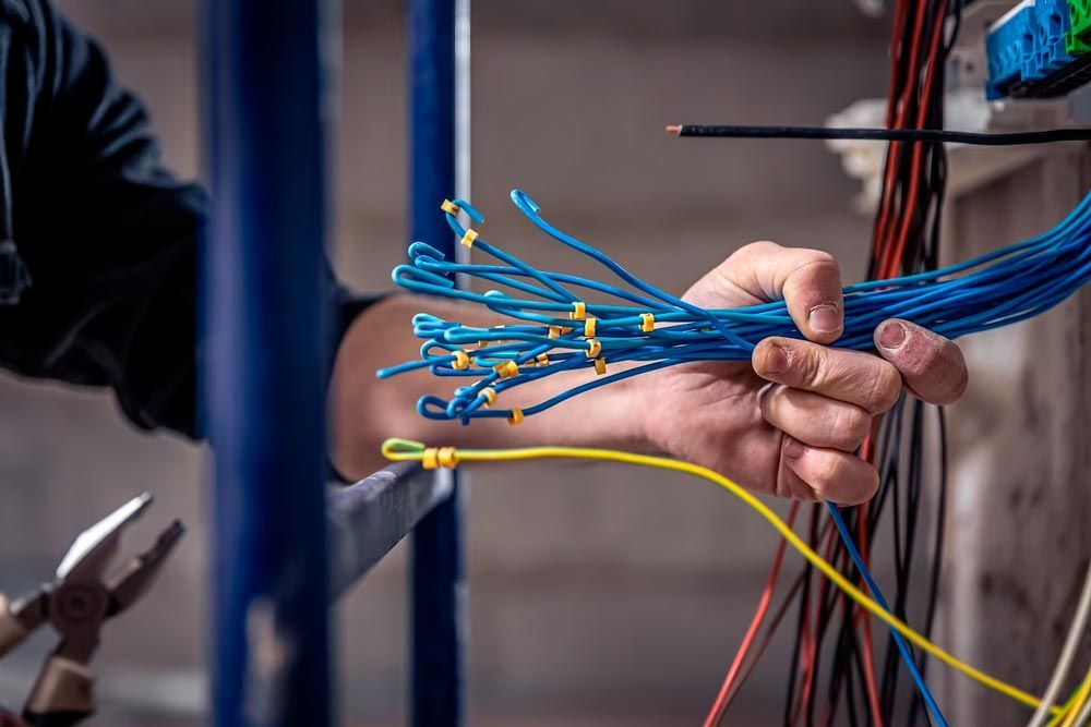 Hand holding blue wires with yellow connectors, near pliers and electrical components.