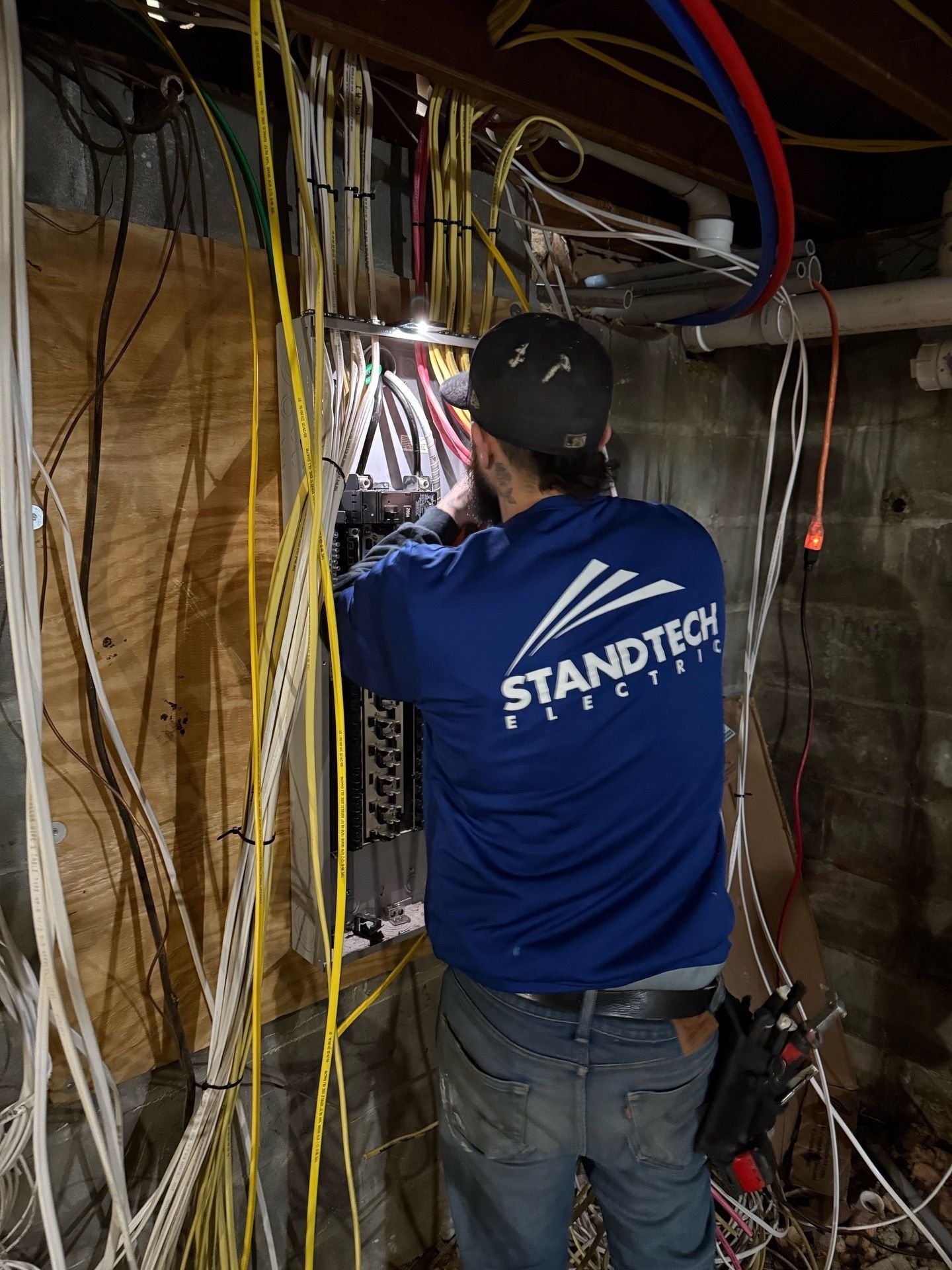 Electrician in a yellow hard hat working on wiring in a room under construction.
