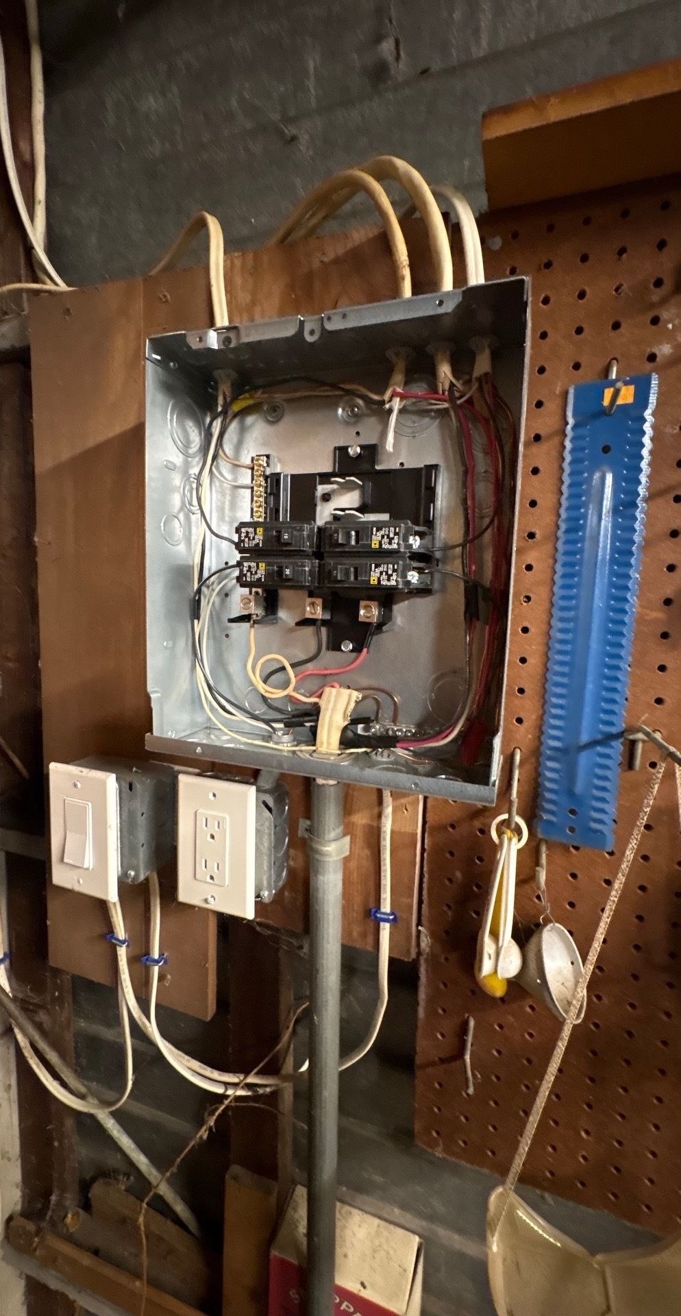 Man in orange work suit and face shield working on electrical panel outdoors.