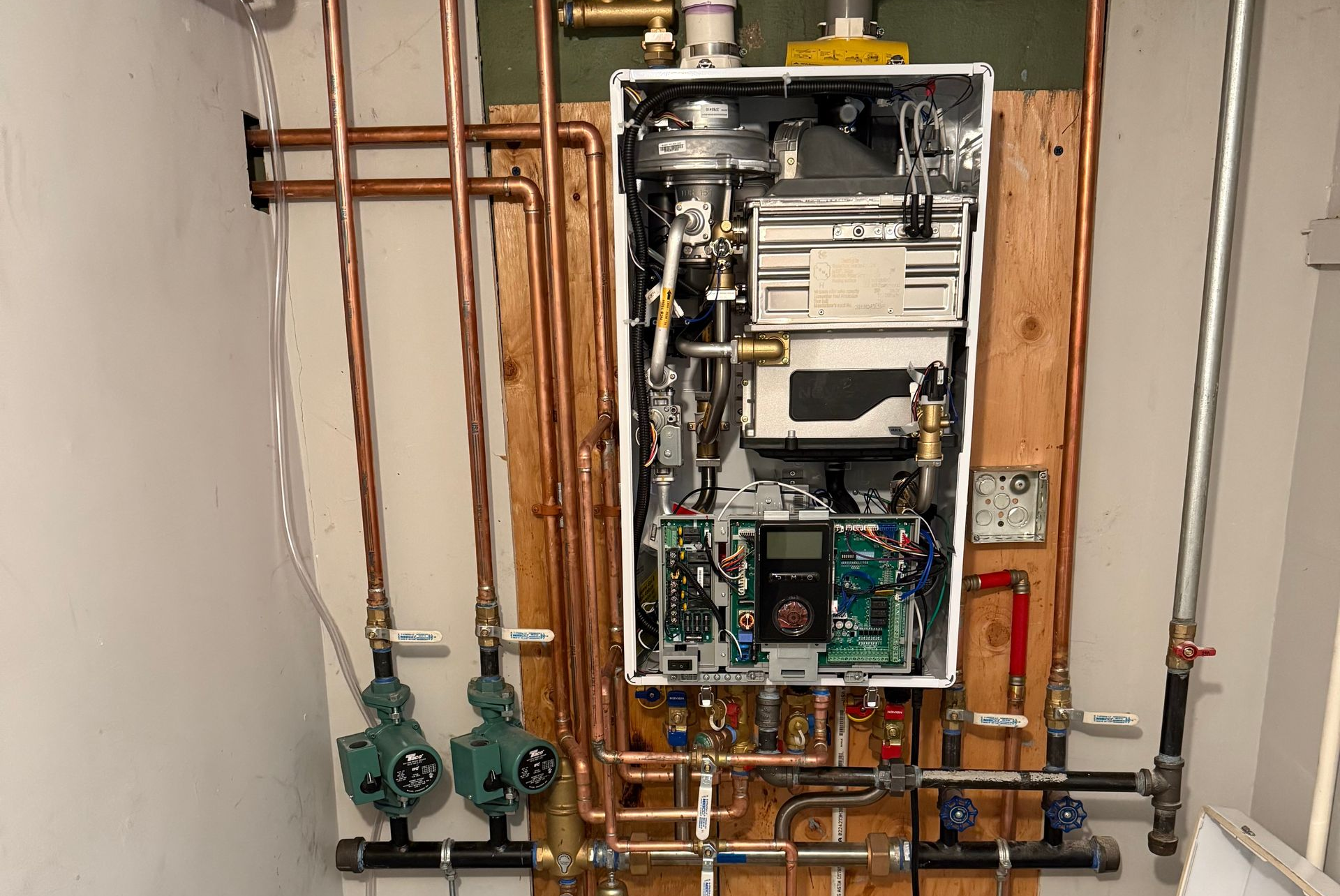 Electrician in a white hard hat and yellow safety glasses tests electrical panel with multimeter.