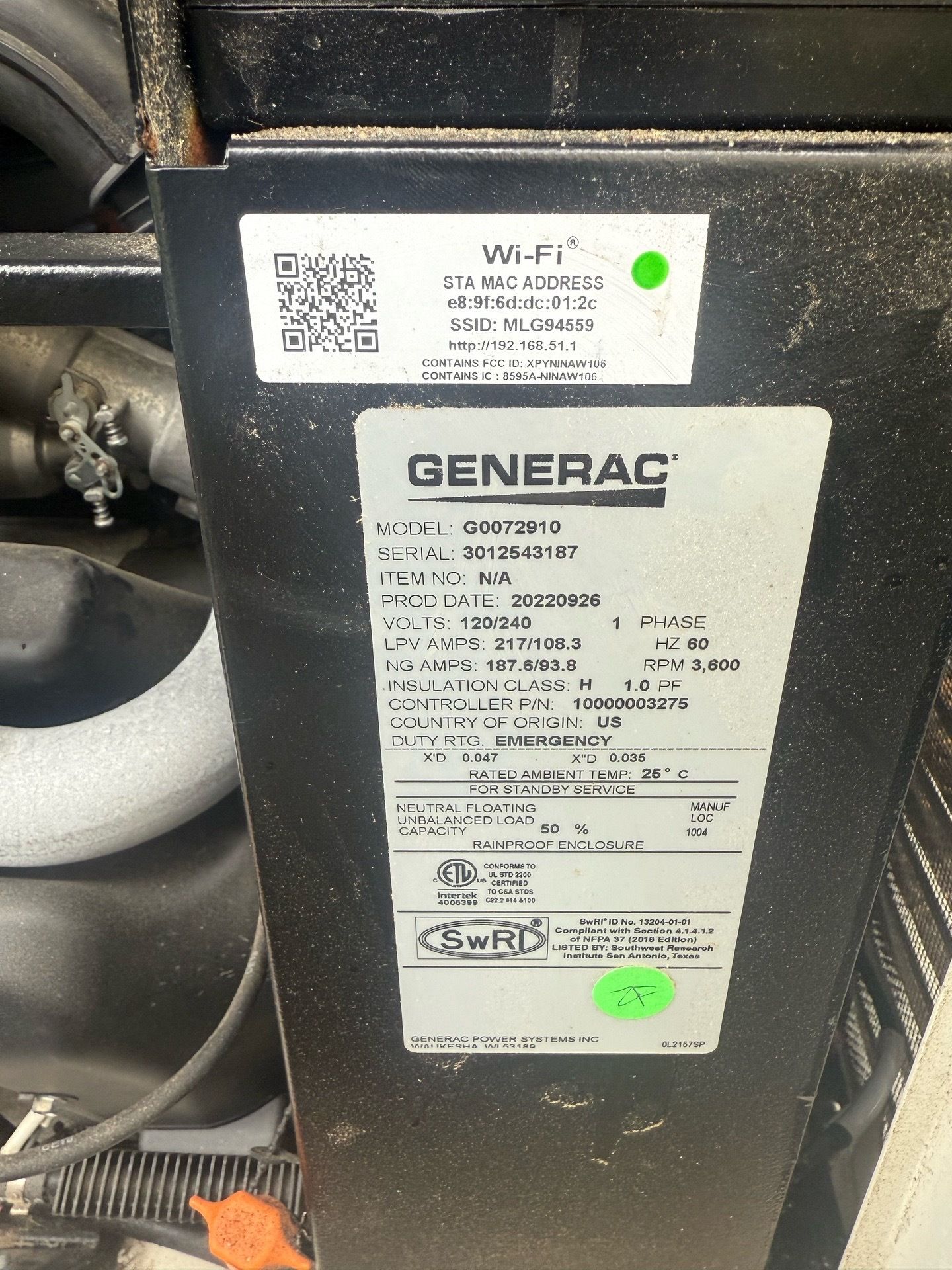 A gray Generac home generator sits outside a brick building amidst landscaping with flowers.