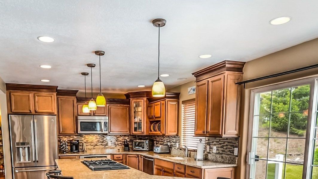 Kitchen with brown cabinets, stainless steel appliances, and pendant lights. A large window provides natural light.