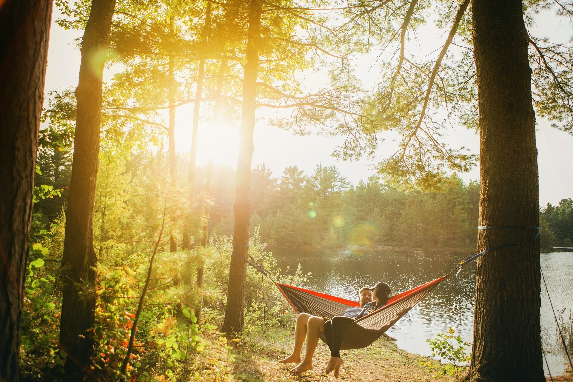Eine Person sitzt in einer Hängematte an einem See im Wald.