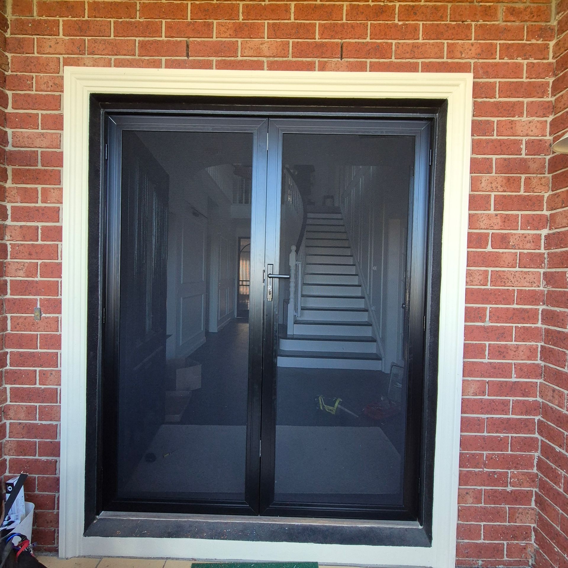 Black-framed security door in a red brick wall, reflecting an interior staircase — Barwon Locksmith & Security Doors in Grovedale, VIC