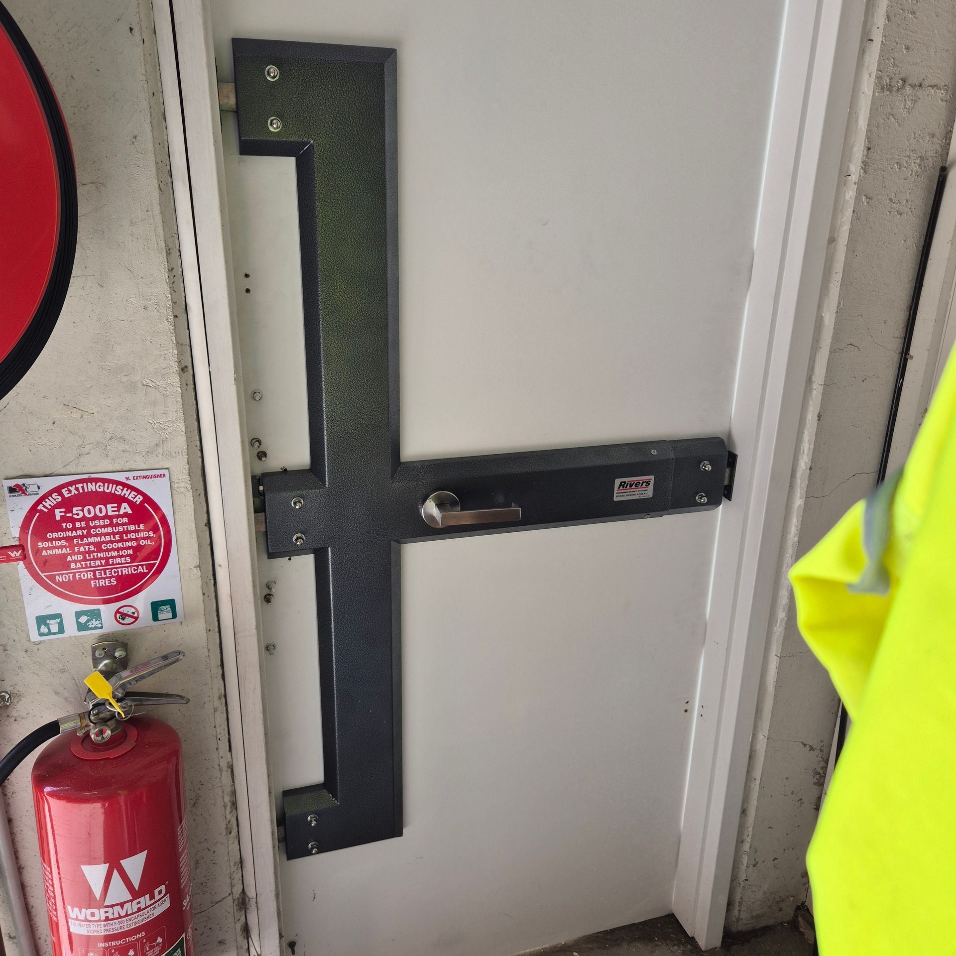 Door secured with a black metal bar lock beside a red fire extinguisher — Barwon Locksmith & Security Doors in Grovedale, VIC