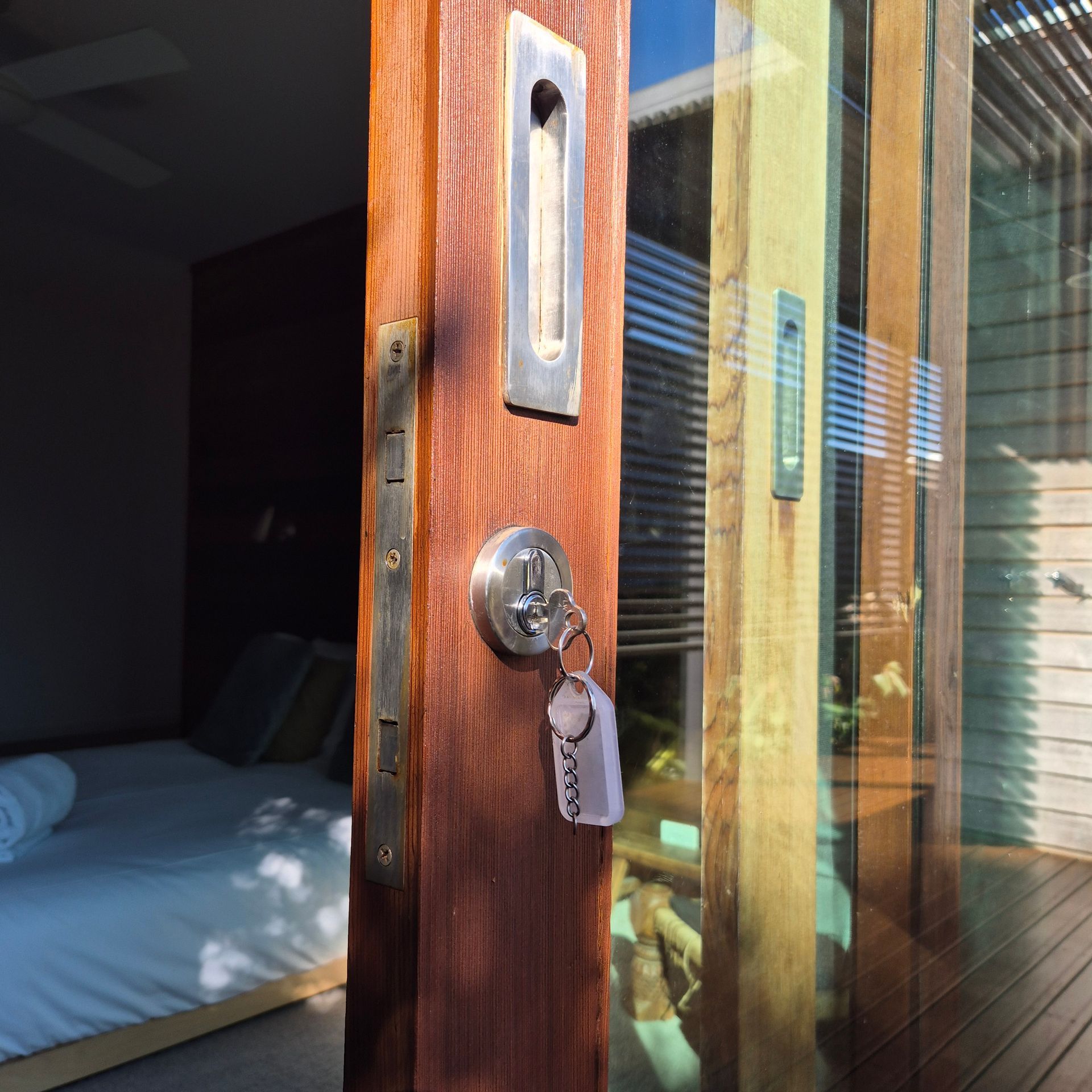 Open wooden door with a silver lock and key, revealing a bedroom with a bed inside — Barwon Locksmith & Security Doors in Grovedale, VIC