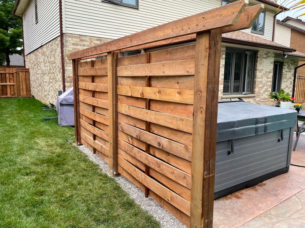 A wooden fence surrounds a hot tub in a backyard.