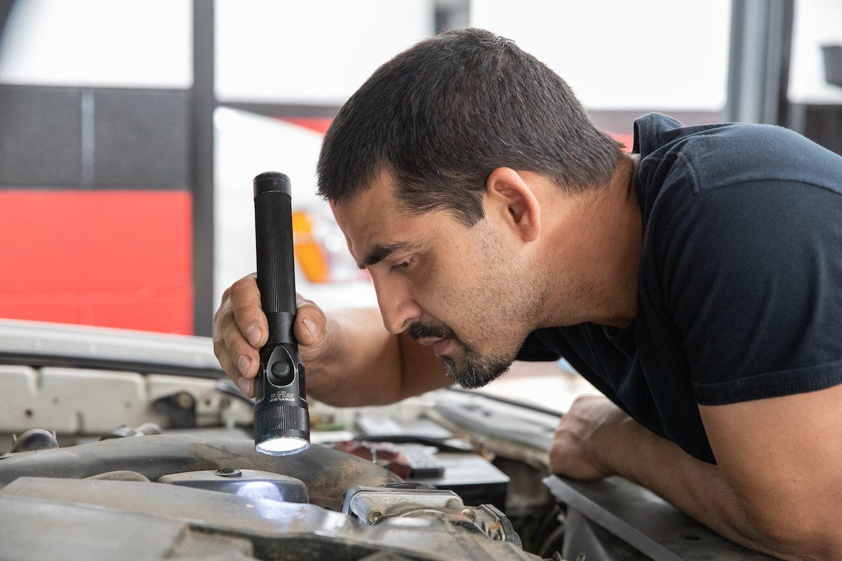 A man is looking under the hood of a car with a flashlight.