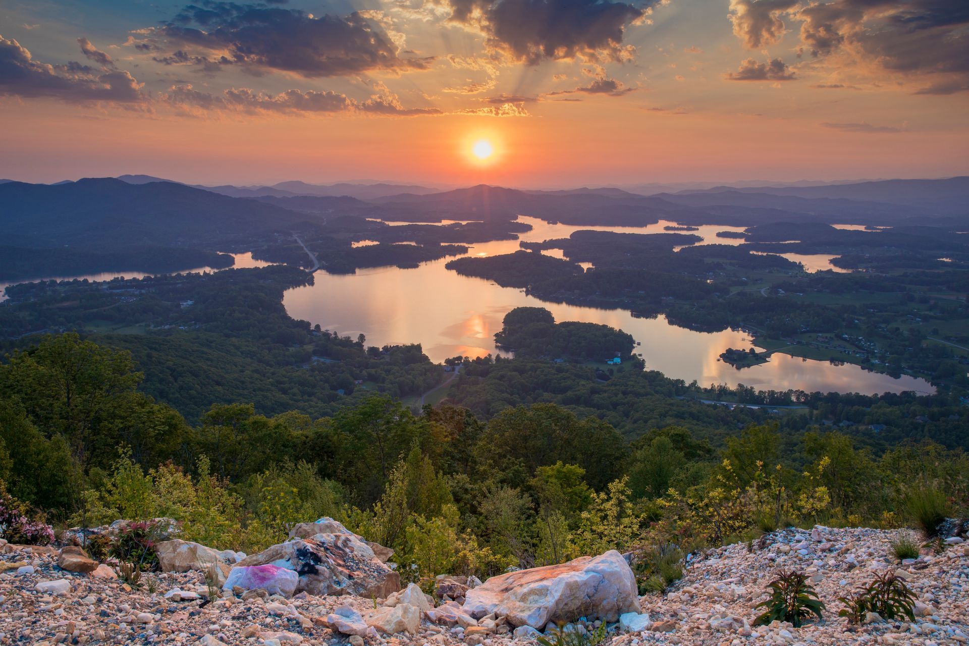 The sun is setting over a lake surrounded by mountains.