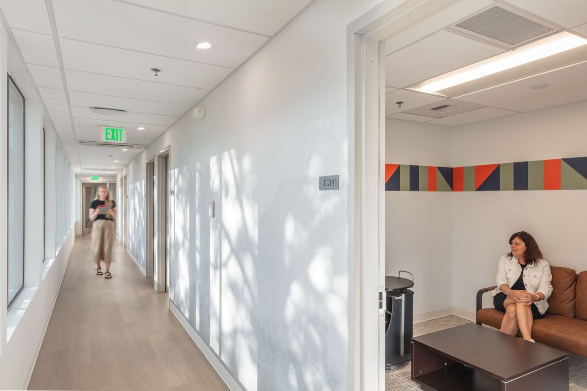 Hallway with a woman walking and another seated in a waiting area with orange and blue artwork.