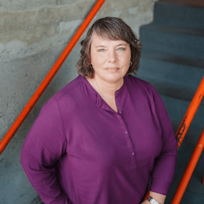 Woman in purple shirt standing by orange railing and concrete stairs.