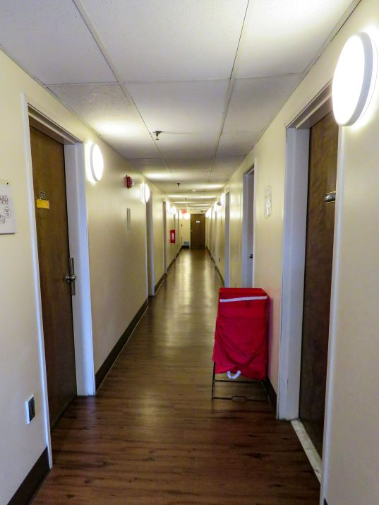 Hallway with wooden floor, doors, wall lights, and a red hamper.