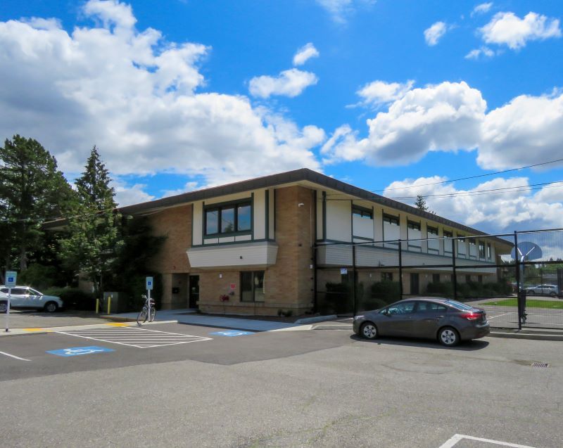 Building with a parking lot and a few cars. A sunny day with blue sky and clouds.