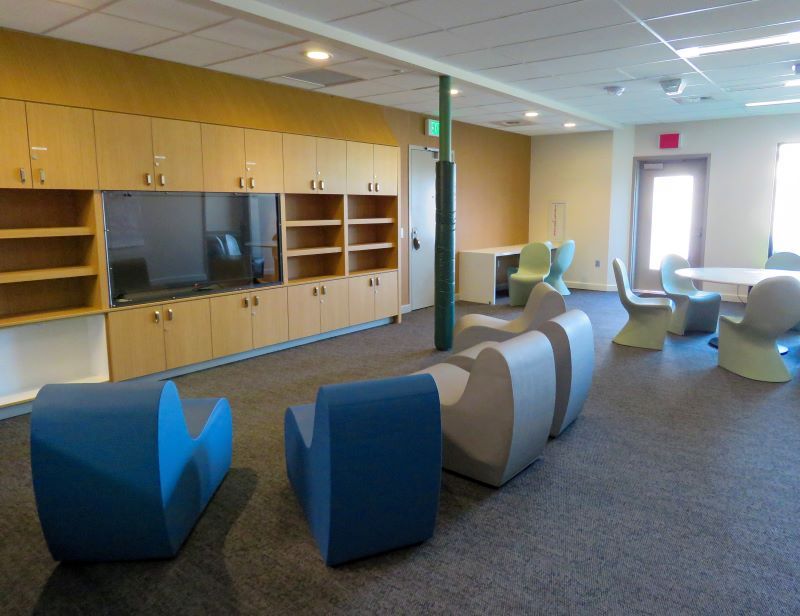 Lounge area with built-in TV, storage cabinets, curved seating, and a table with chairs.