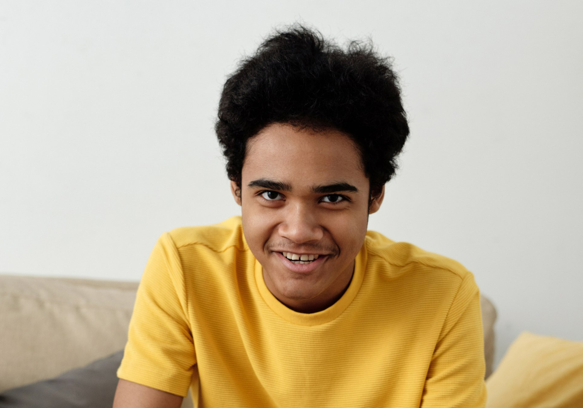 Young person with dark, curly hair and a yellow shirt smiles at the camera.