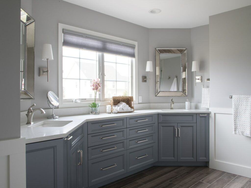 A bathroom remodel with gray cabinets, dual sinks, two mirrors and a window.