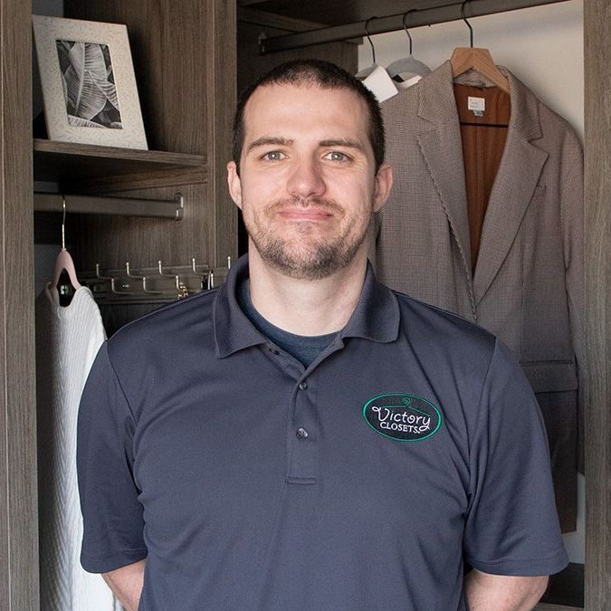 A man in a blue shirt is standing in a closet.