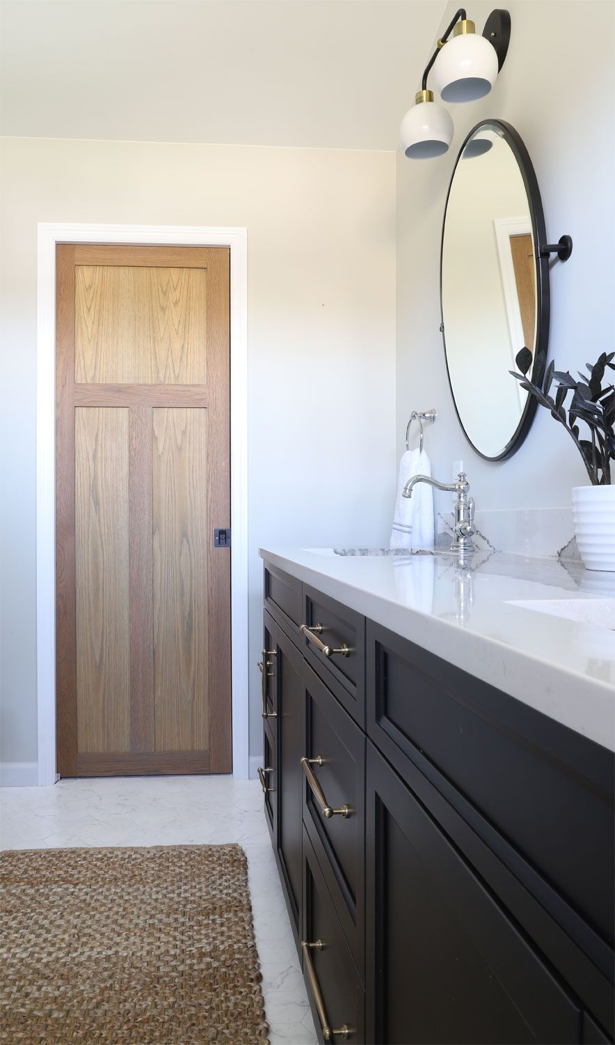Bathroom with a dark wood vanity, white countertop, oval mirror, and wooden door.