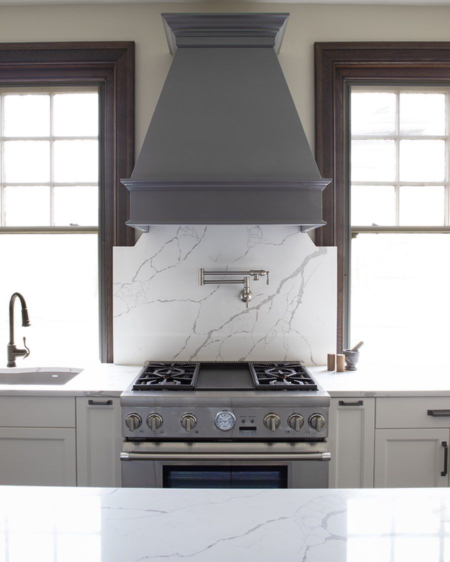 A kitchen with a stove , sink , and hood.
