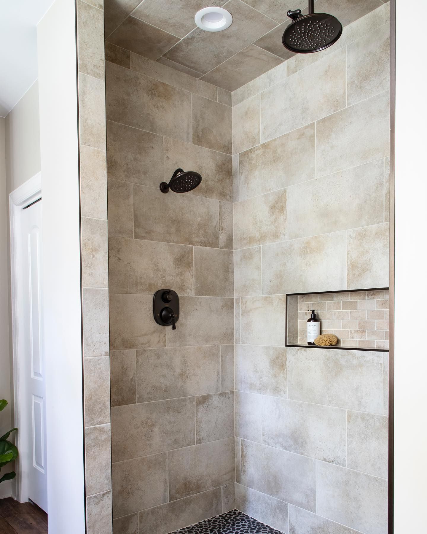 A bathroom with a walk in shower with two shower heads and a shelf.