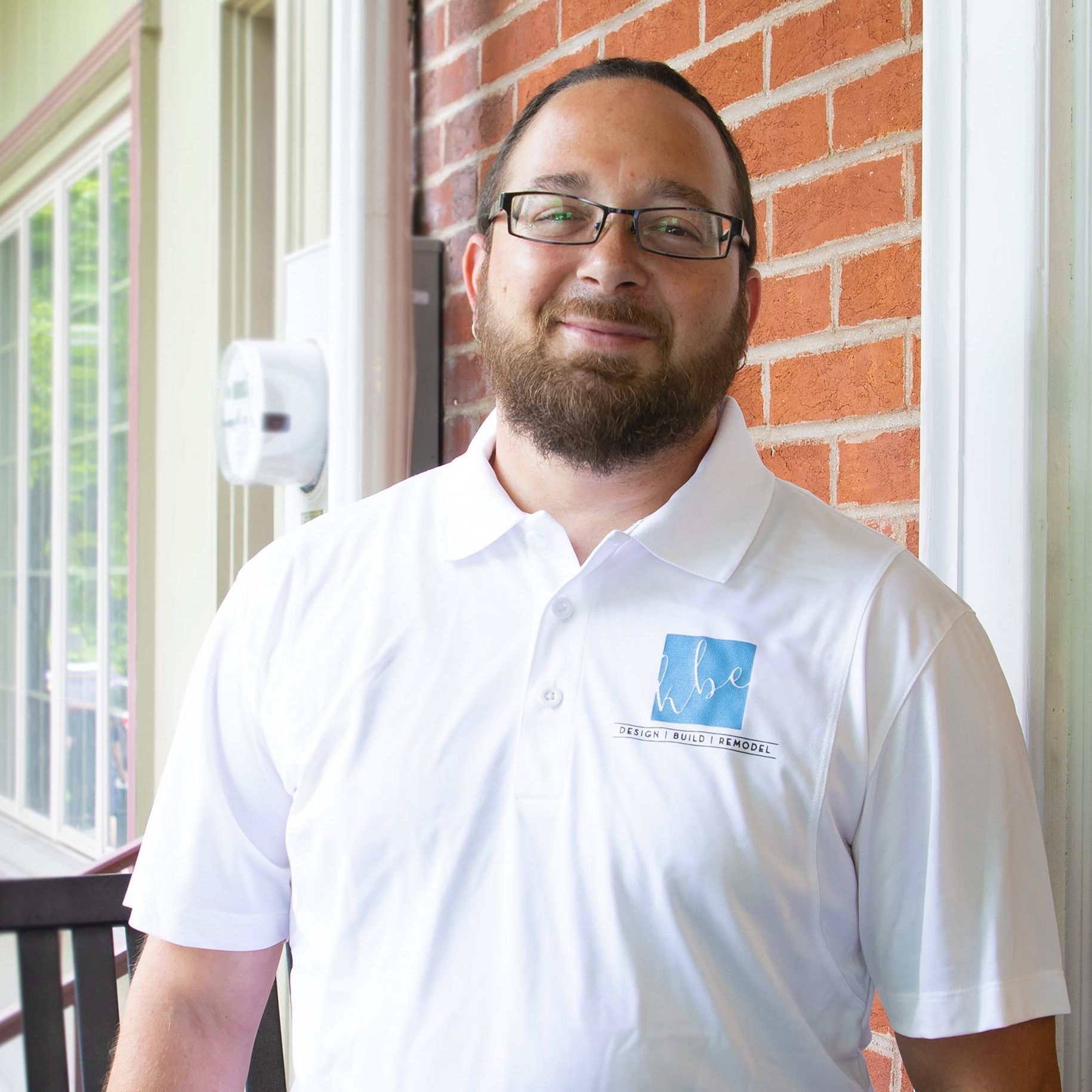 A man with a beard wearing glasses and a white polo shirt
