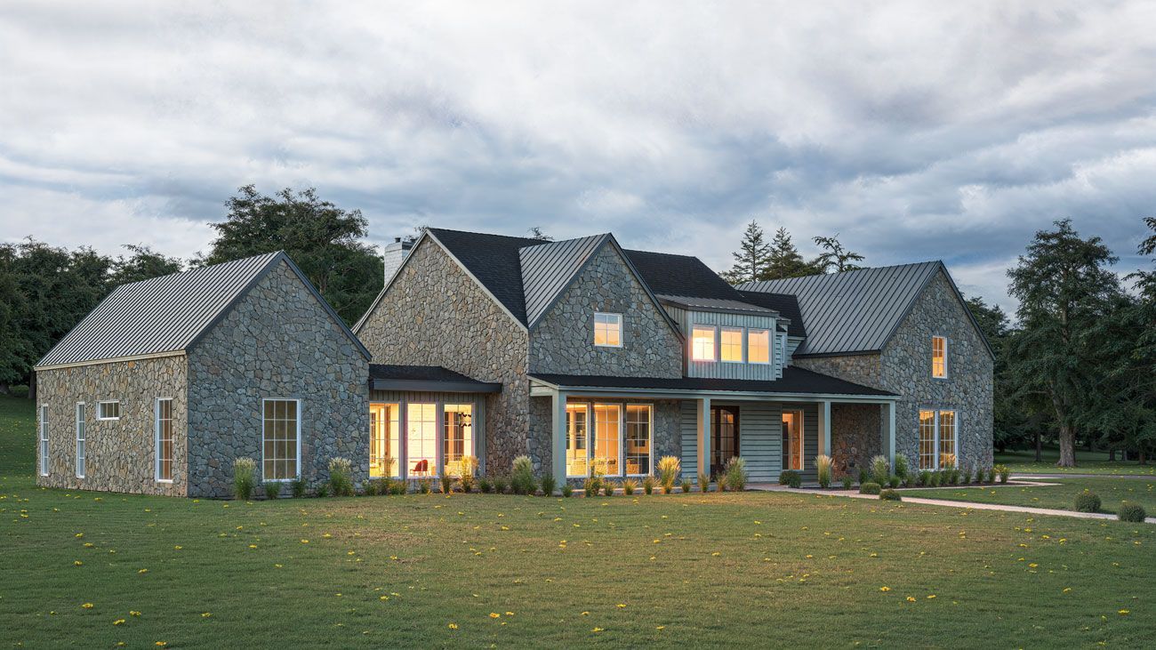 A large house with a lot of windows is sitting on top of a lush green field.