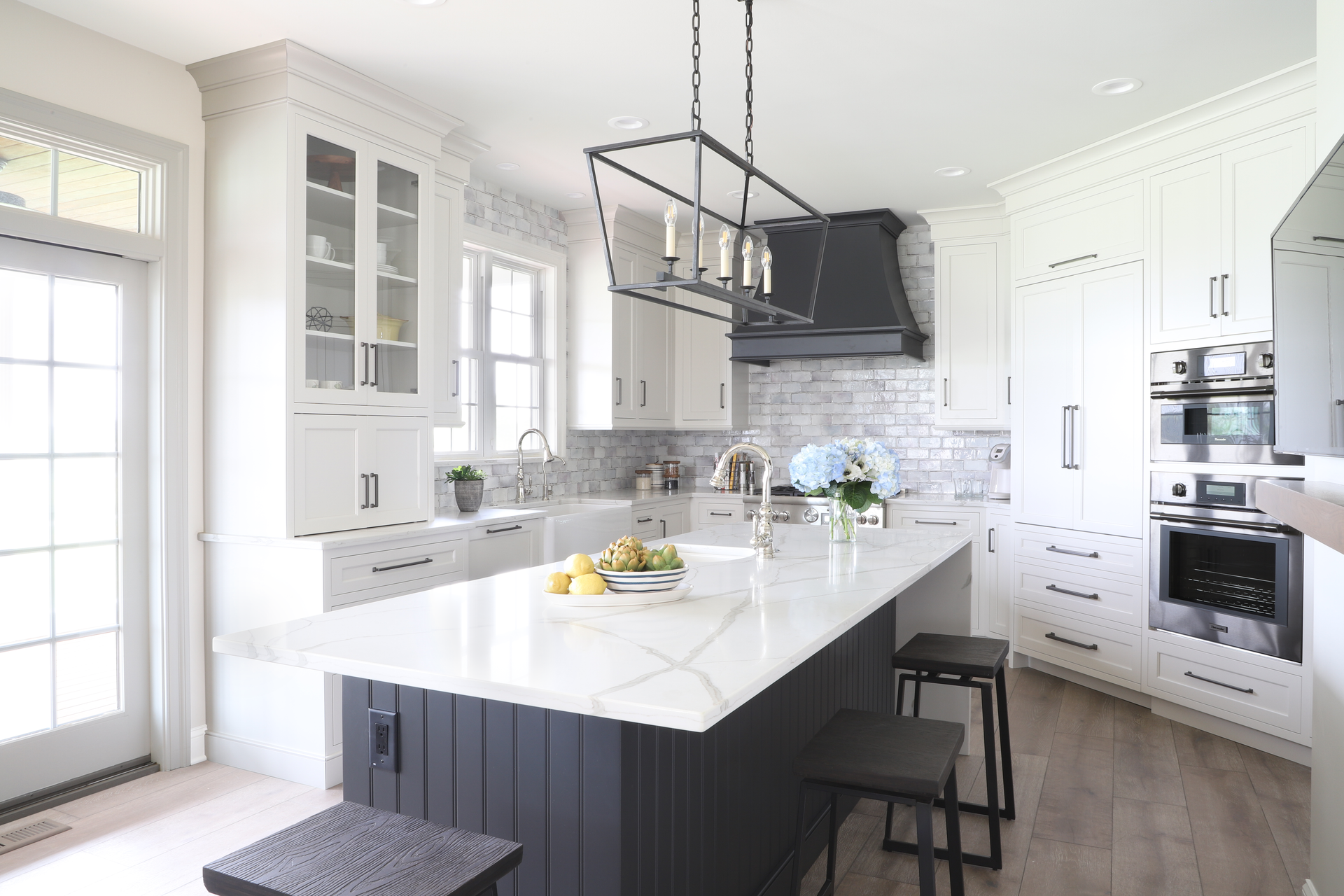 White and gray kitchen with a large island, black accents, and pendant lighting.