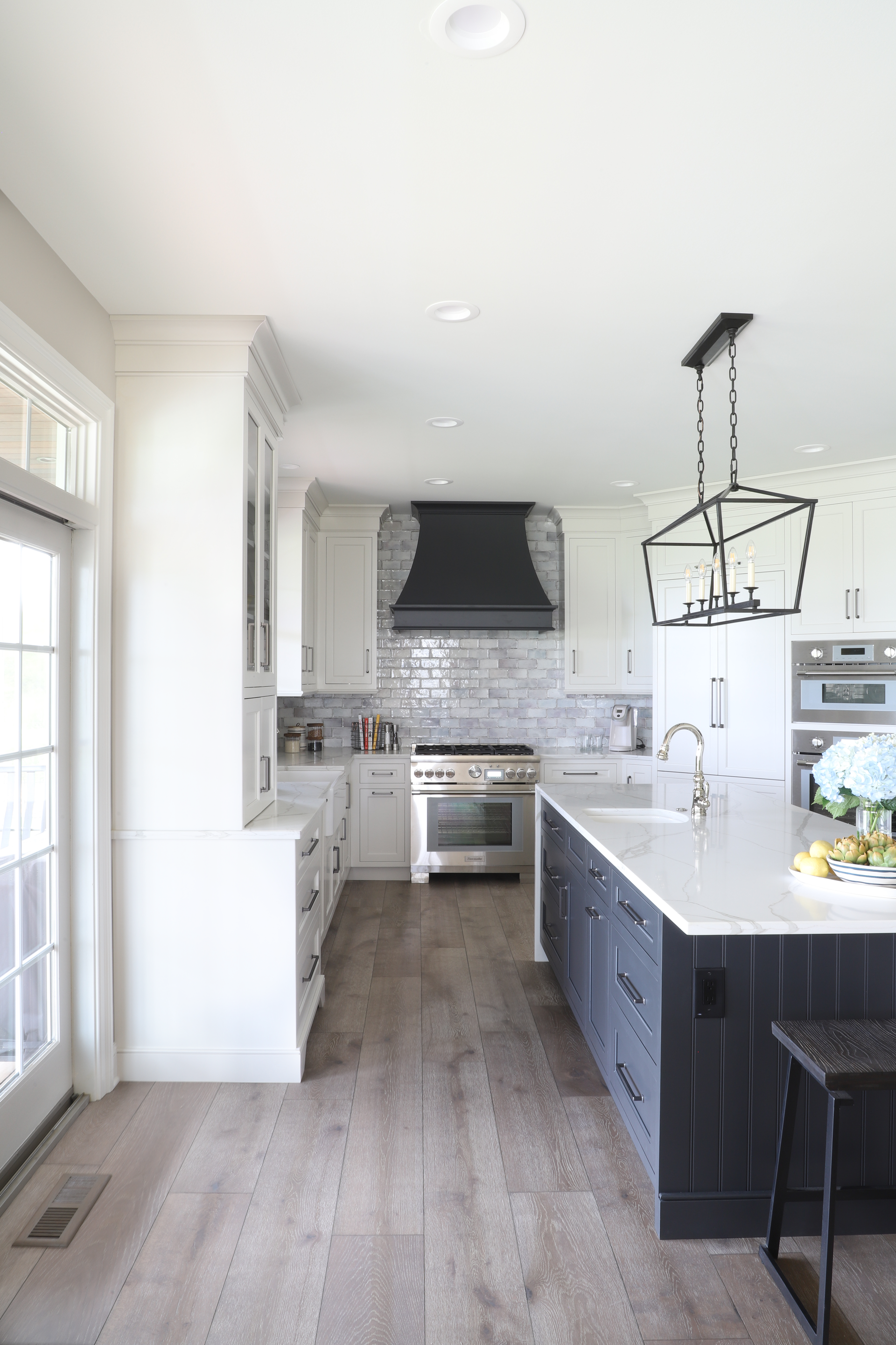 Modern white kitchen with a dark blue island, stainless steel appliances, and wood flooring.