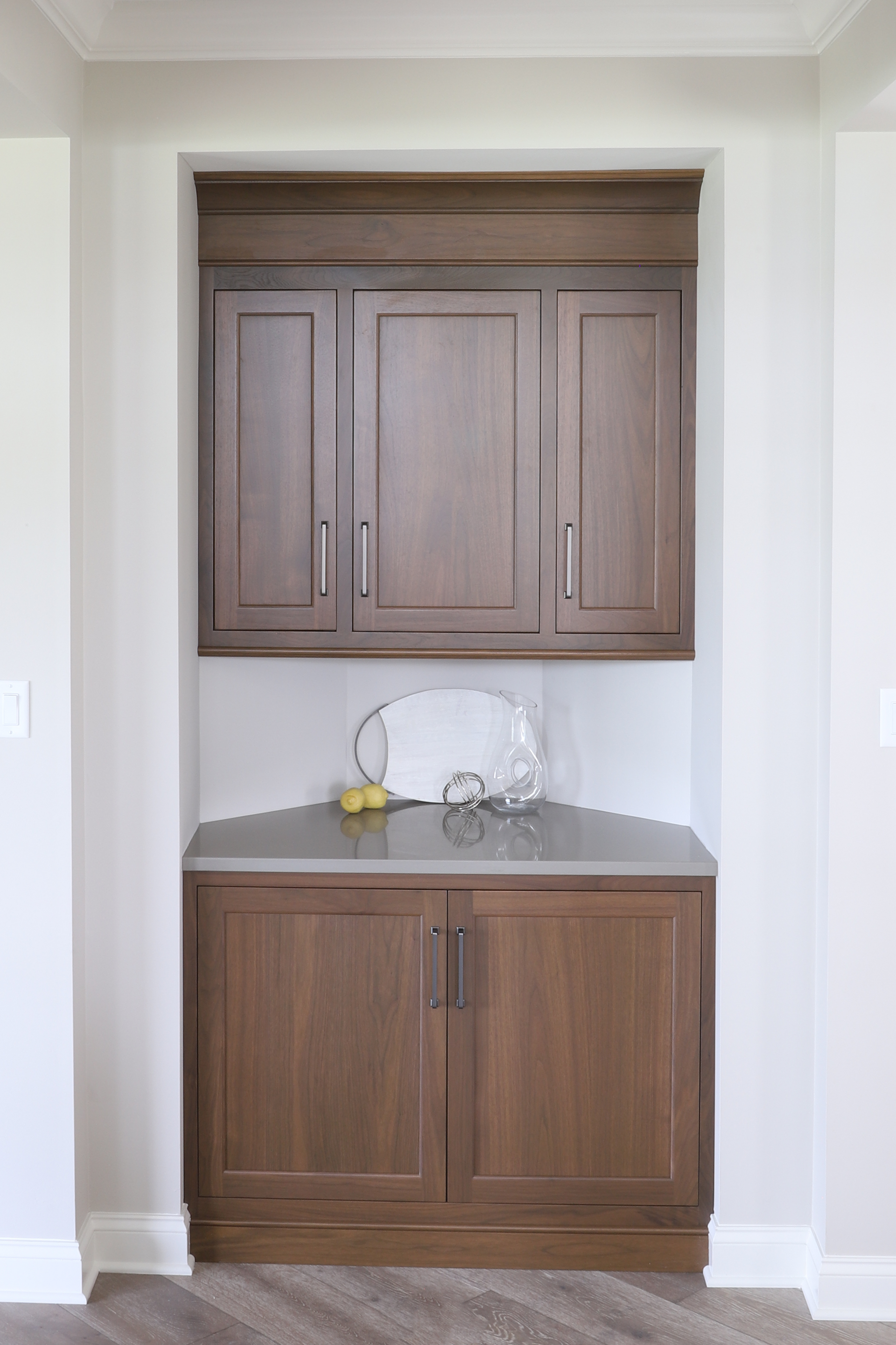 Built-in wooden cabinetry in a recessed wall niche. Cabinets are brown with a gray countertop and white walls.