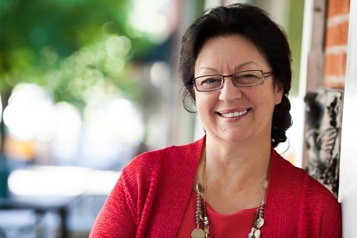 A woman wearing glasses and a red sweater is smiling for the camera.