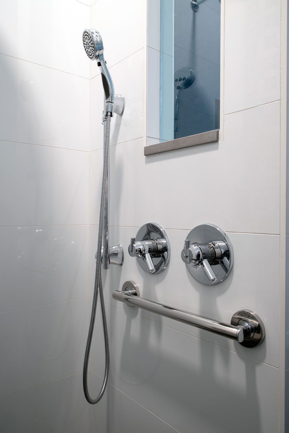 A shower with a hand rail and a mirror on the wall.