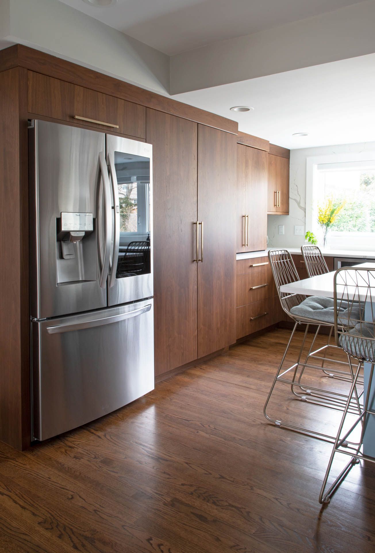 A modern kitchen featuring a stainless steel refrigerator, dark wood cabinets, and bar stools near a window.