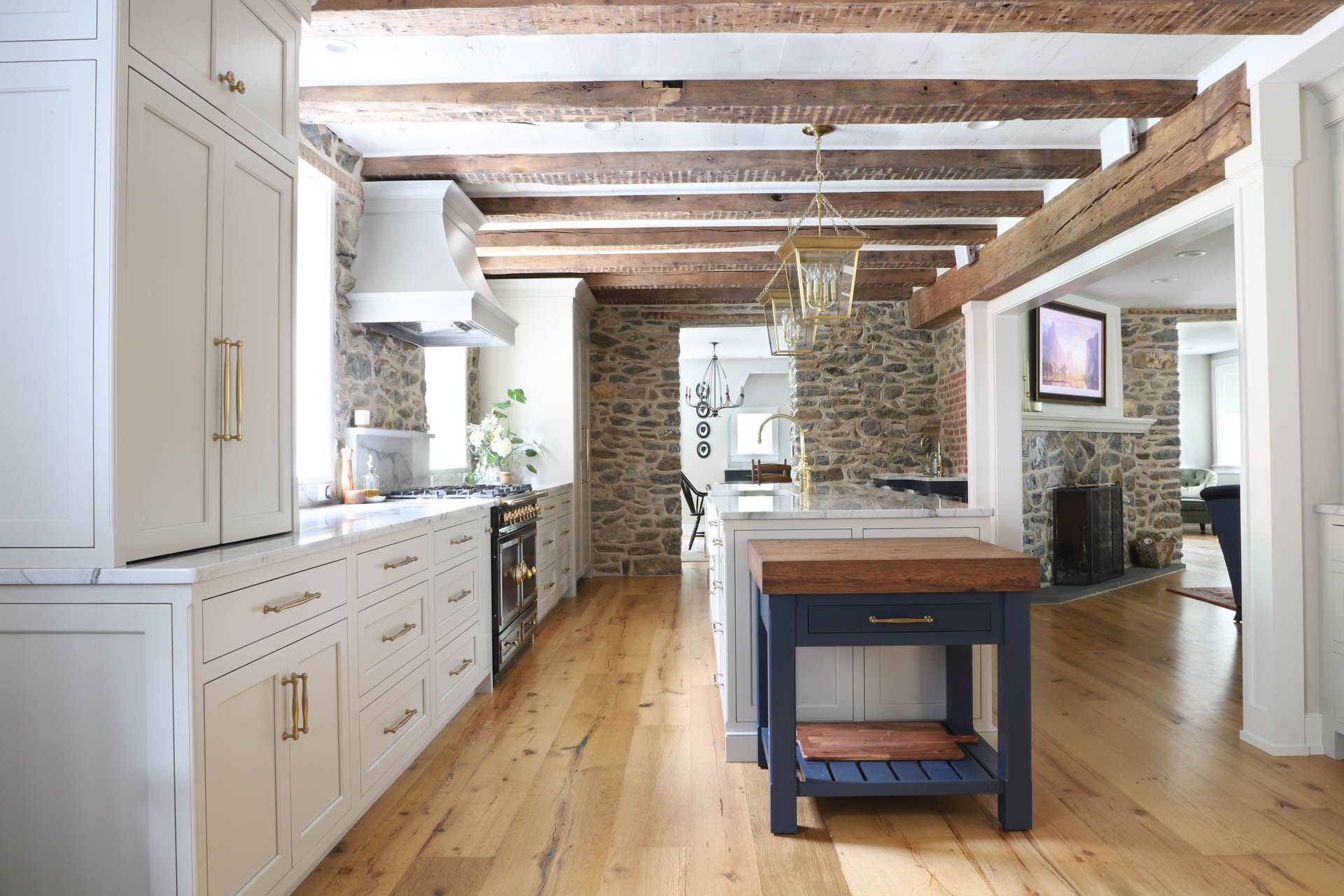 Kitchen with stone walls, wood beams, light wood floors, white cabinets, and a blue island.