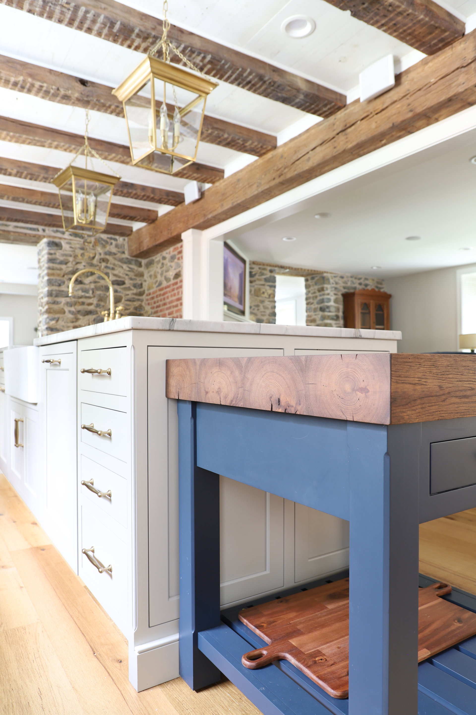 Kitchen with a blue island, wood countertop, white cabinets, and exposed wooden beams.