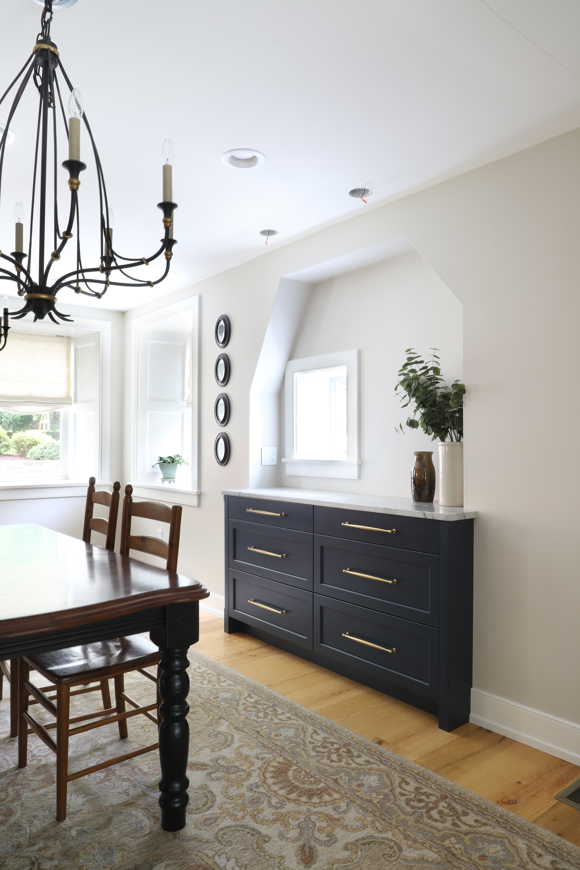 Dining room with a dark blue credenza, wooden table, chandelier, and patterned rug.